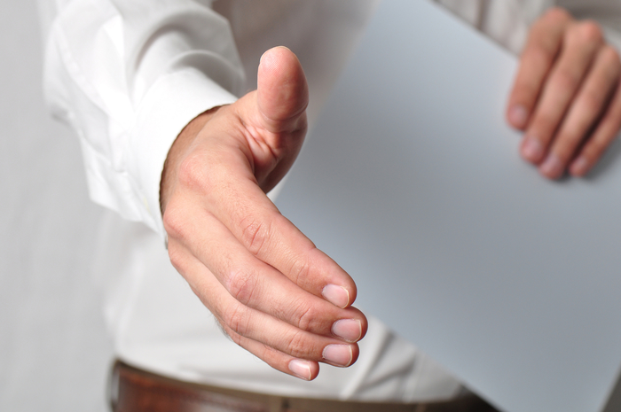 man extending hand for handshake holding paper in other hand